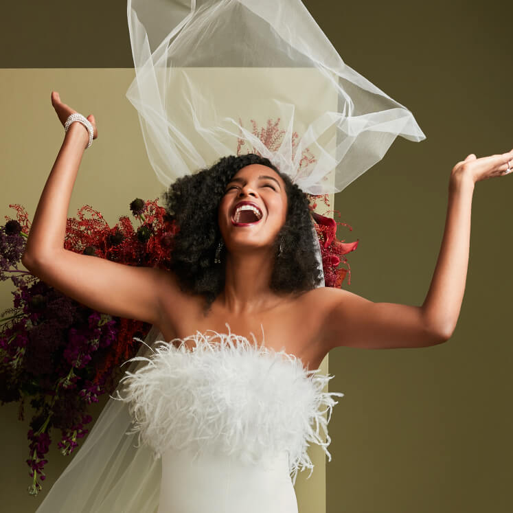 bride in wedding dress and veil smiling with arms raised