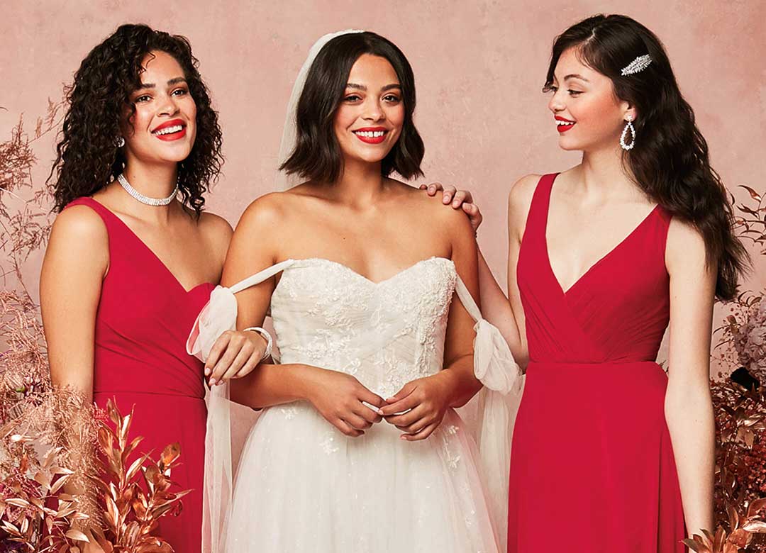 bride with 2 bridesmaids wearing red surrounded by flowers