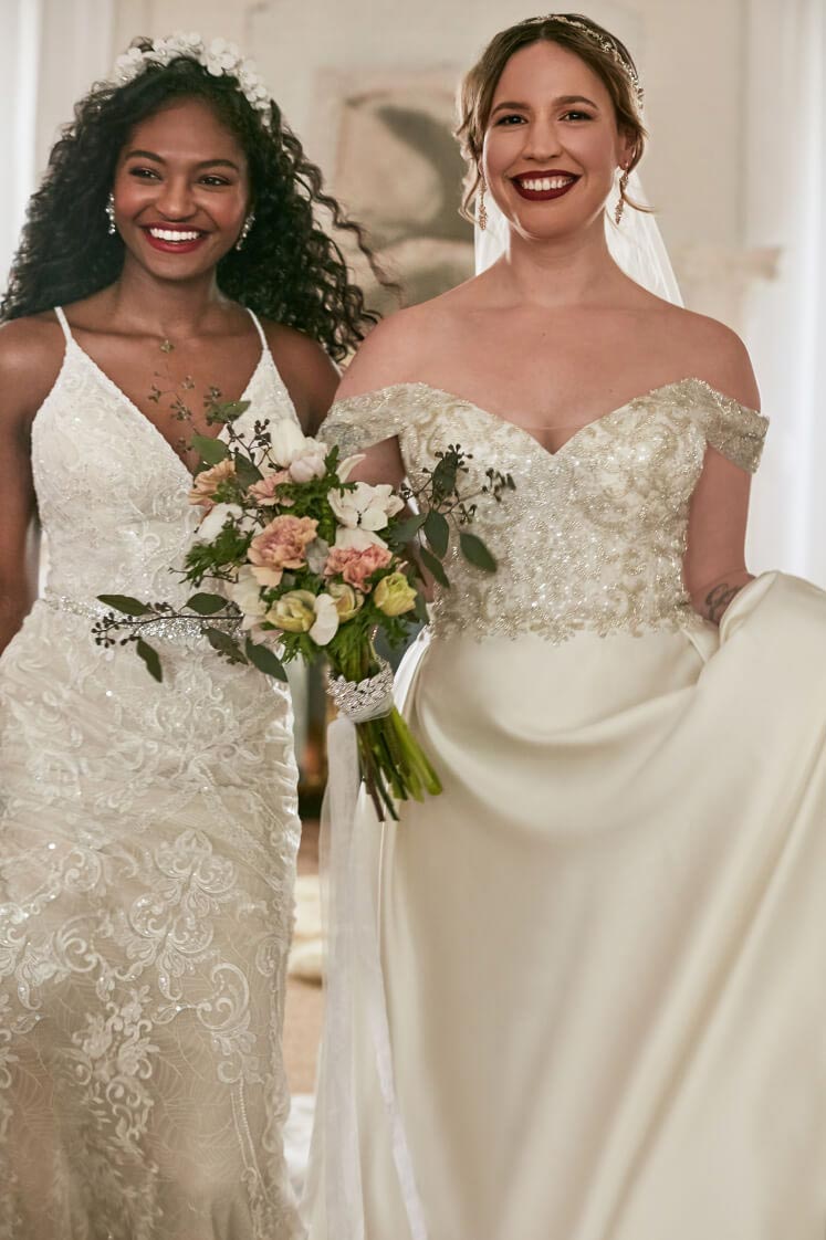 2 brides wearing wedding dresses walking and holding a bouquet