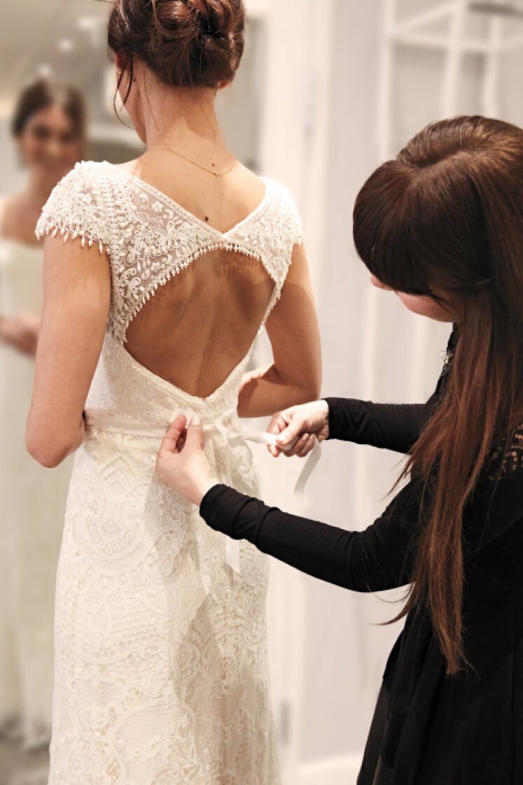 store associate tying back of wedding dress on bride