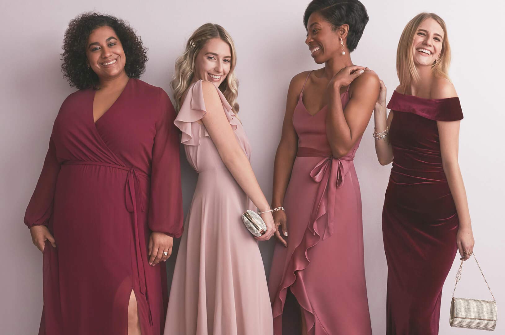 4 bridesmaids wearing different red dresses standing next to each other smiling