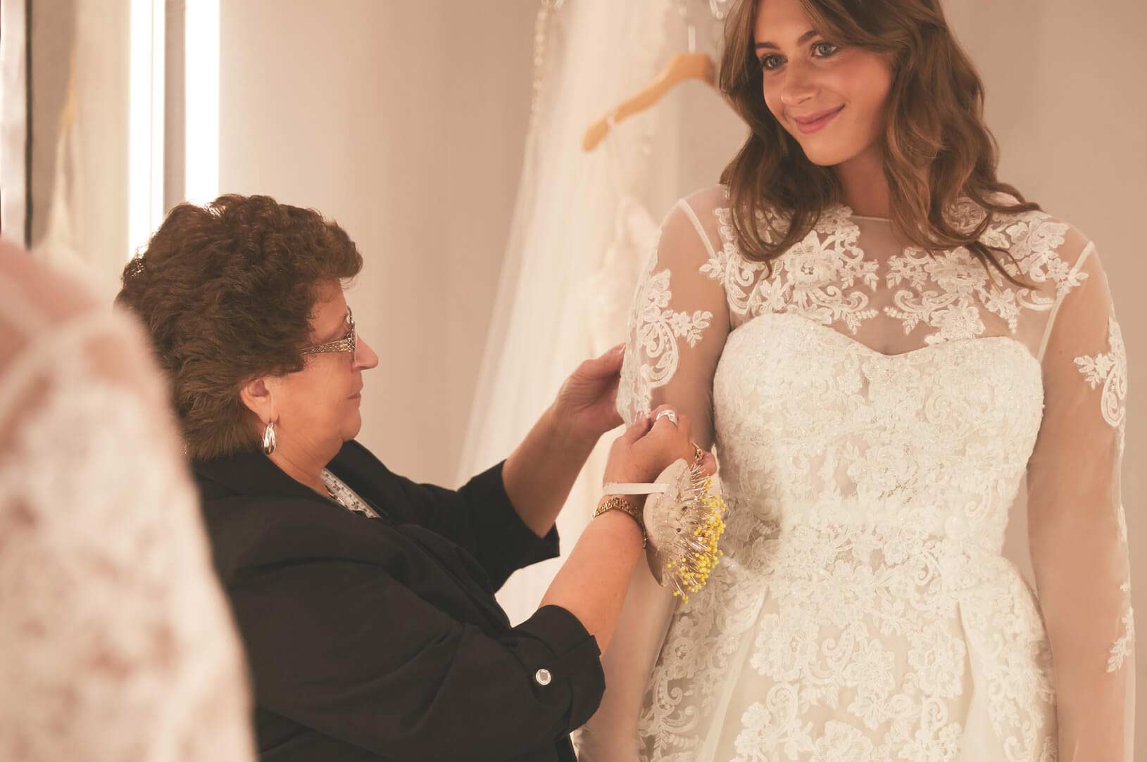 store associate adjusting sleeve on wedding dress on bride