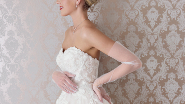 woman wearing a wedding dress and long gloves standing in front of a wallpapered hallway