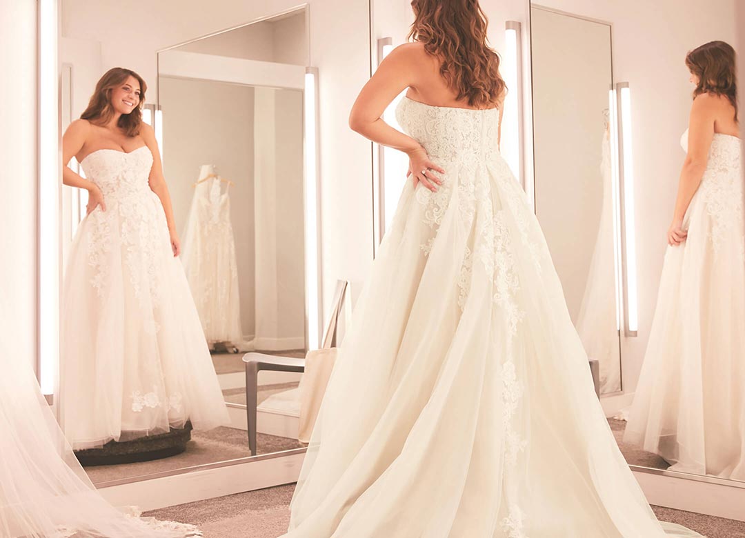 bride in a wedding dress standing in front of a mirror in a store