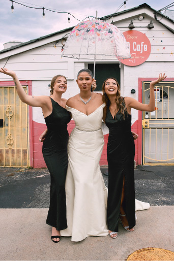bride with her two bridesmaids outside holding an umbrella
