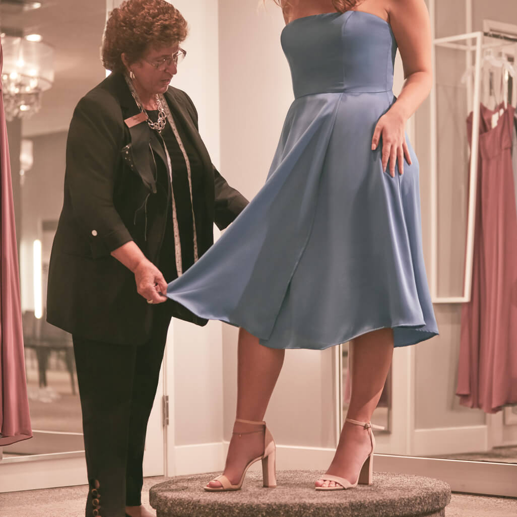 store associate assisting a bridesmaid with a dress fitting