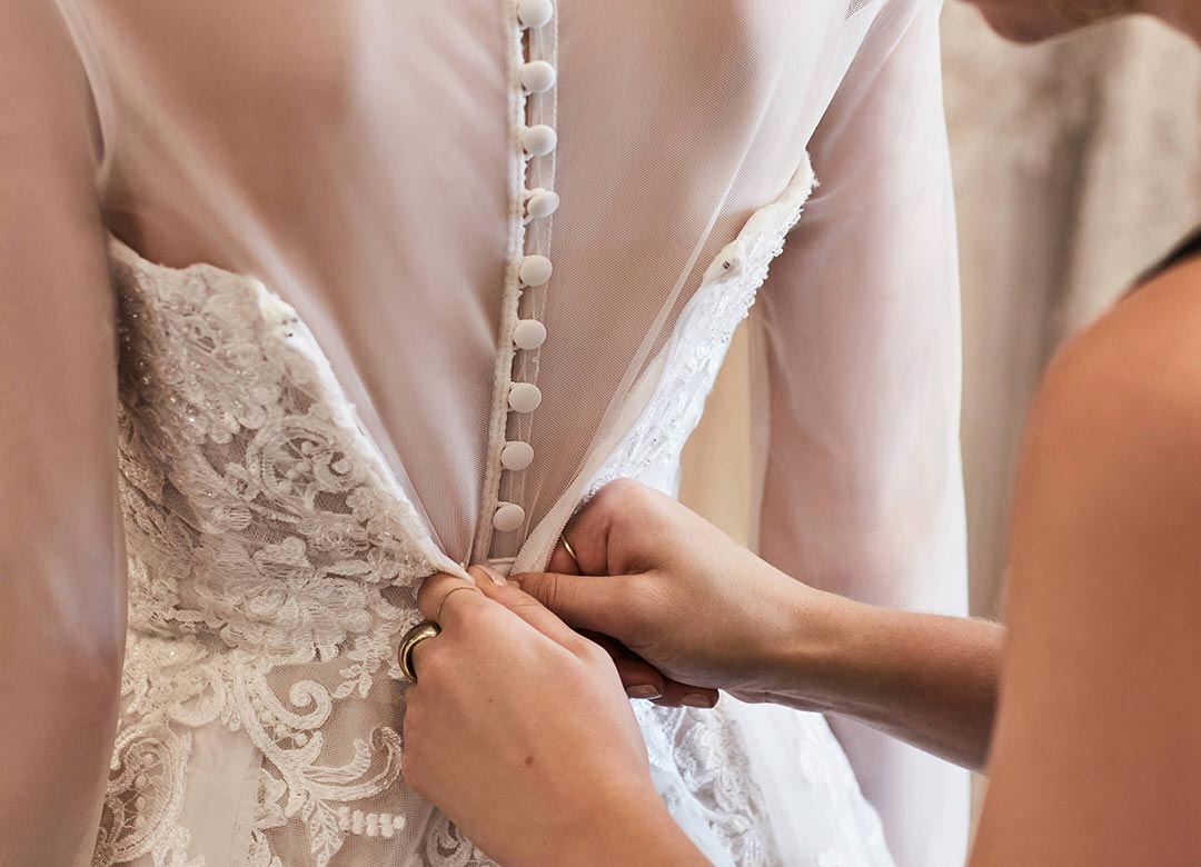 store associate helping bride with wedding dress fitting