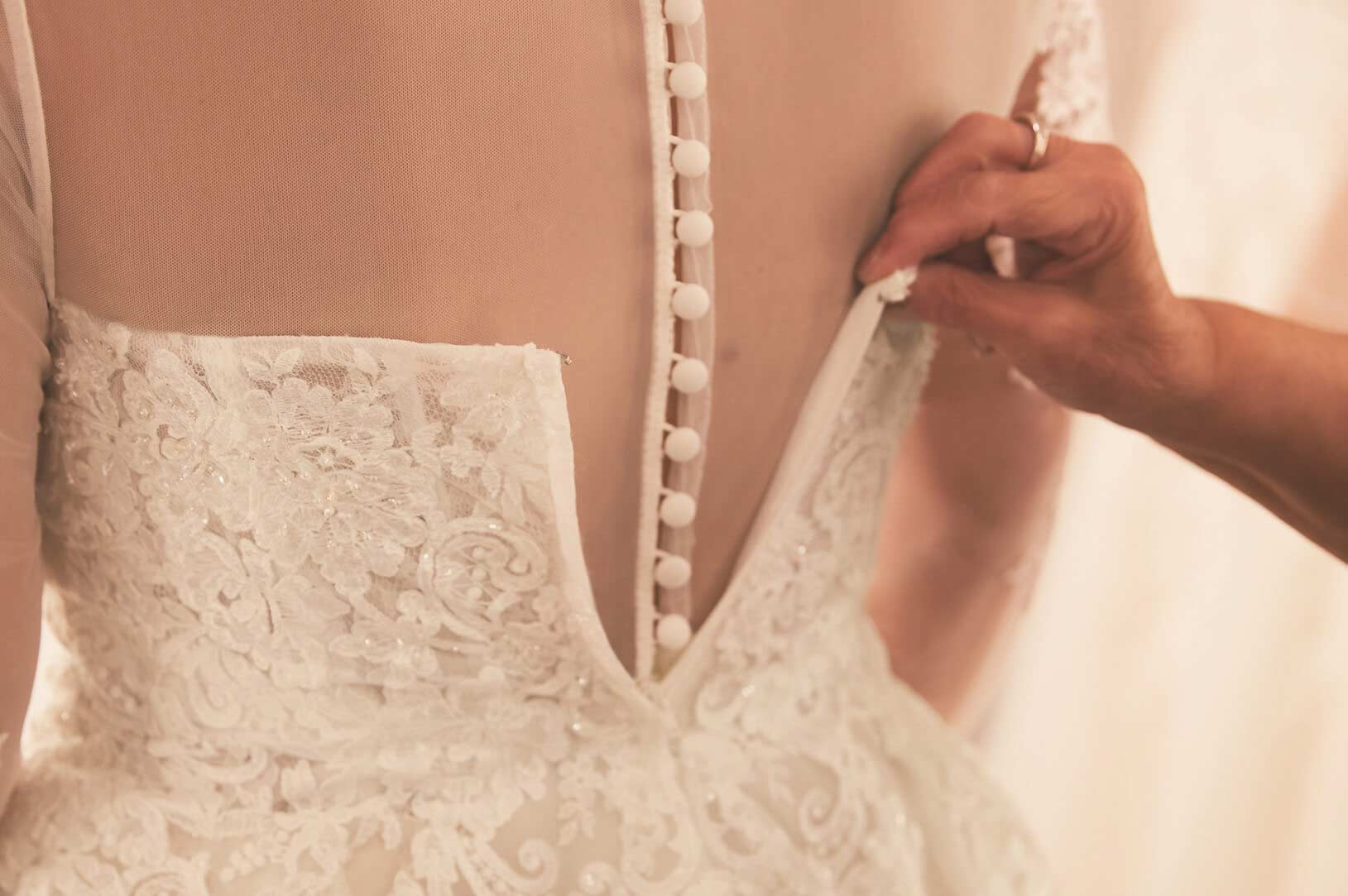 store associate buttoning back of wedding dress on bride