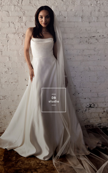 woman in wedding dress standing against a white brick wall
