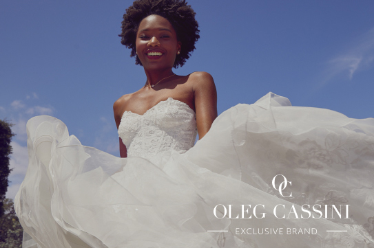 smiling bride holding up wedding gown promoting oleg cassini exclusive brand