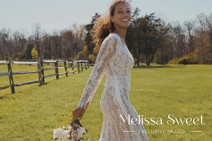 bride in long sleeve wedding dress walking in a field and holding flower bouquet