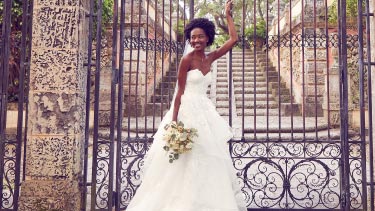 bride wearing wedding dress and veil standing in front of gate holding flower bouquet
