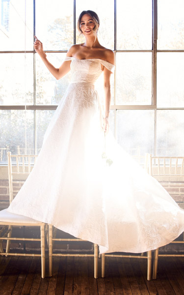 woman in wedding dress standing on chairs in front of a window