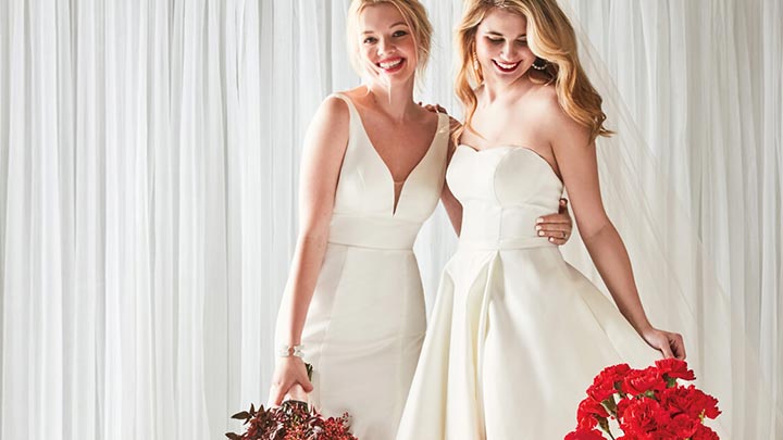 2 brides standing in front of white curtains with flowers around them