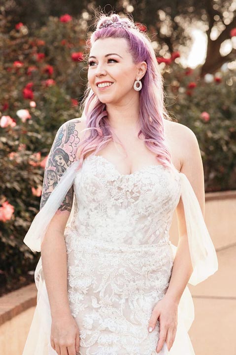 smiling bride wearing a wedding dress outside with flowers behind her