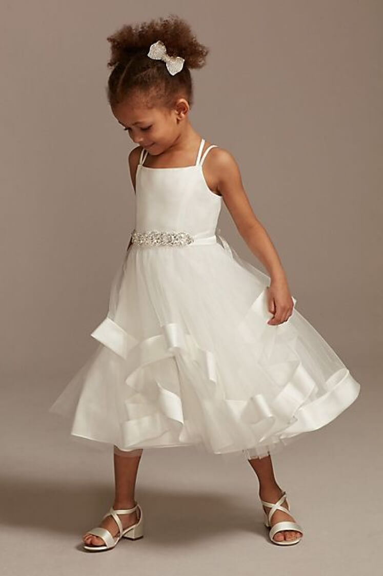 flower girl in a sleeveless satin dress wearing a hair bow looking down to the ground