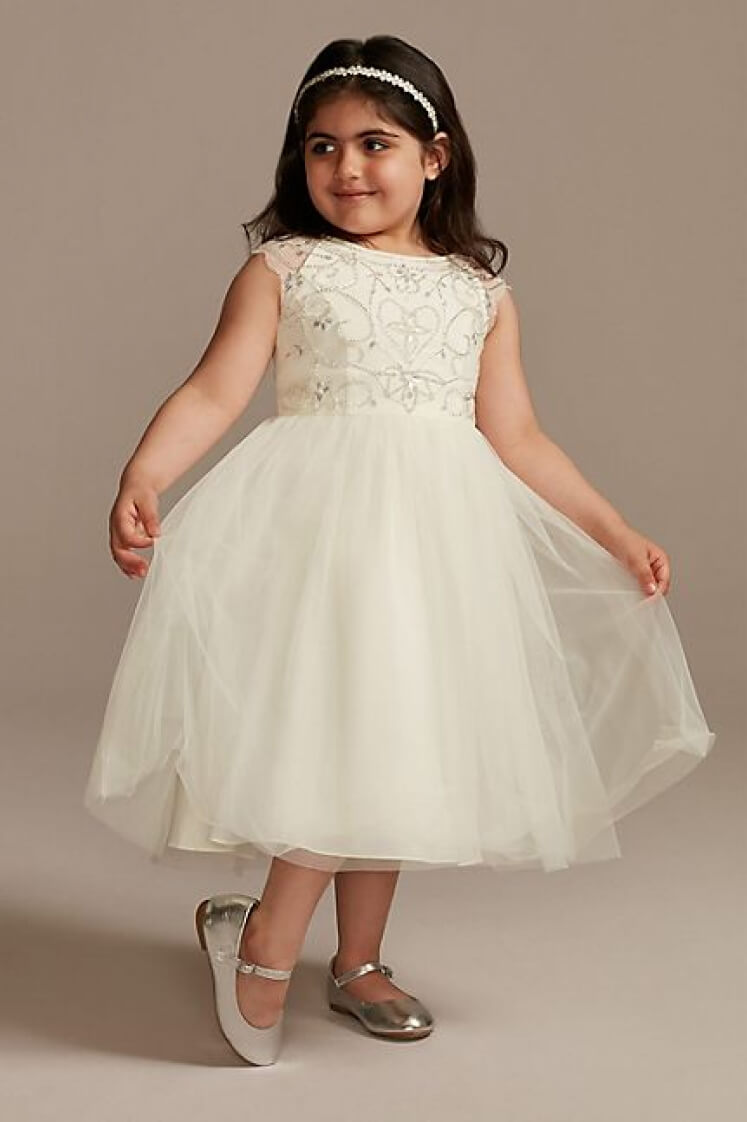 flower girl in a beaded dress wearing a headband standing and holding out dress