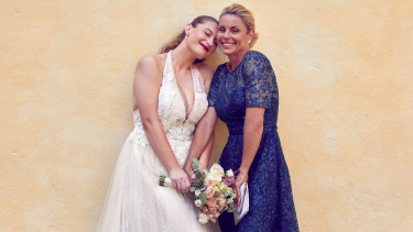 bride holding flower bouquet standing next to mother wearing a blue dress