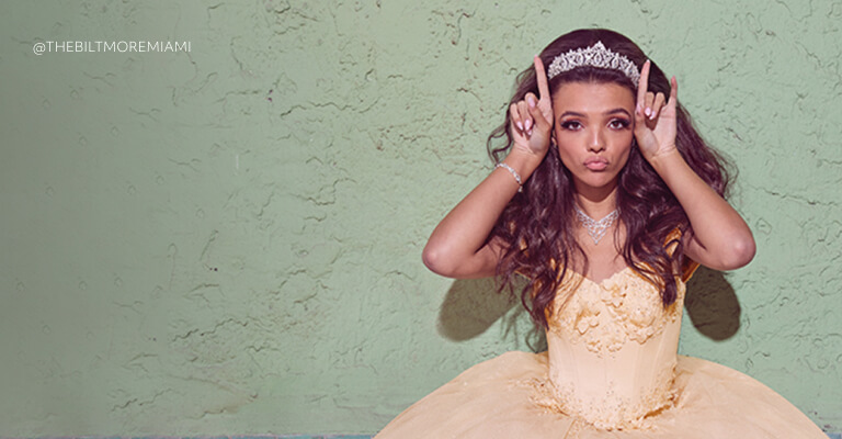 young woman wearing a quinceanera dress and veil holding up fingers next to head