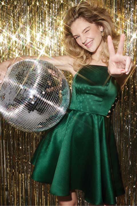 Girl in green prom dress holding a disco ball and flashing a peace sign