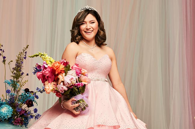 teenage girl smiling wearing a pink ball gown and tiara holding colorful flowers
