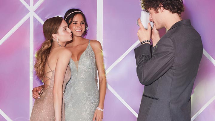 2 girls in different silver dresses getting picture taken by boy in a gray suit jacket