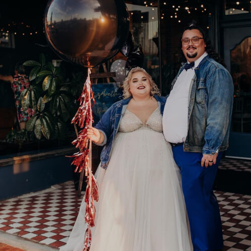 bride and groom standing outside holding large balloon