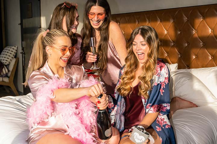 group of women sitting on a bed drinking champagne