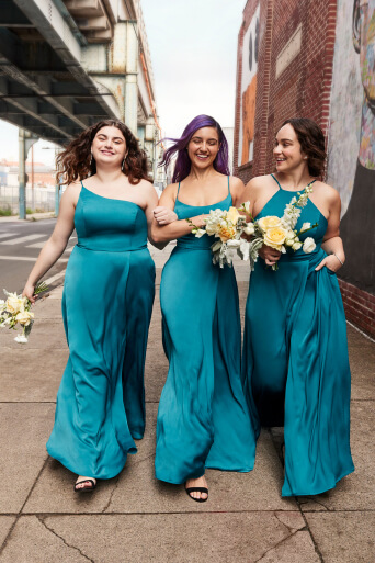 3 bridesmaids in bliss dresses walking arm and arm down the sidewalk