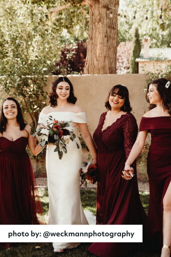 bride holding hands with bridesmaids wearing maroon dresses