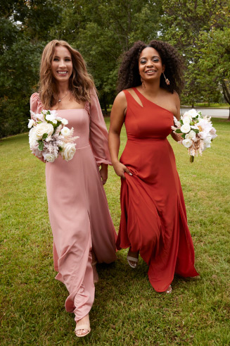 2 bridesmaids walking through a field holding bouquets