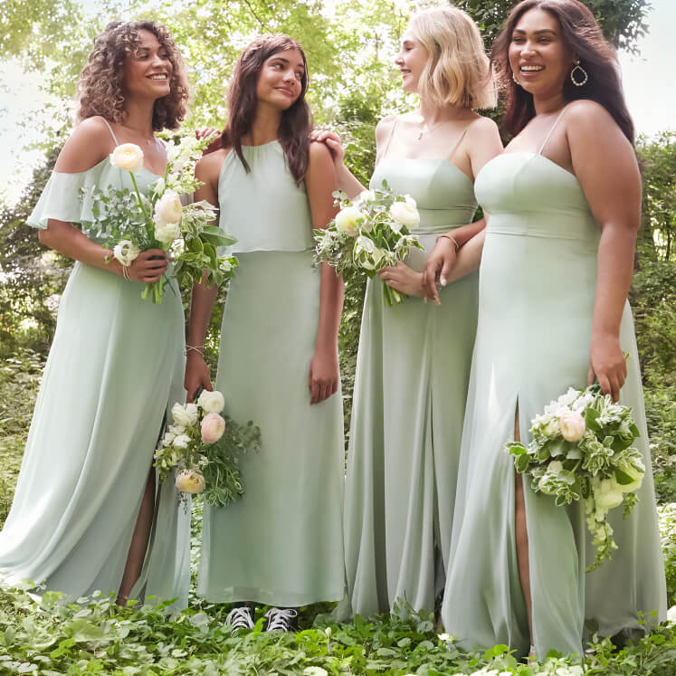 four bridesmaids in green dresses standing together and holding flower bouquets
