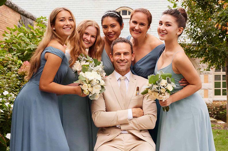 groom sitting with bridesmaids in blue dresses standing around