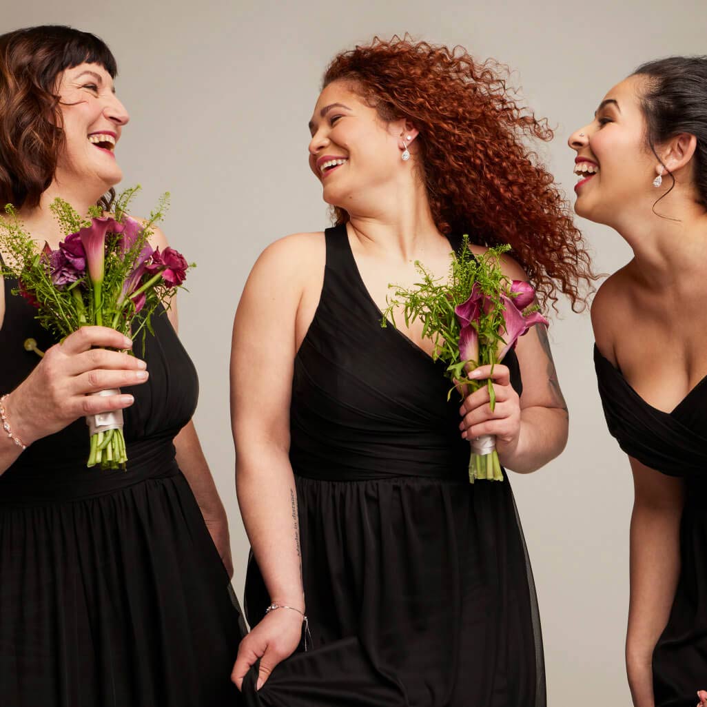 three bridesmaids in black dresses laughing and holding flowers