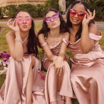 three bridesmaids sitting outside with their heart shaped sunglasses