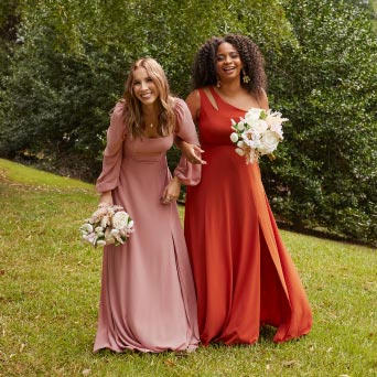 two bridesmaids outside in a park holding bouquets