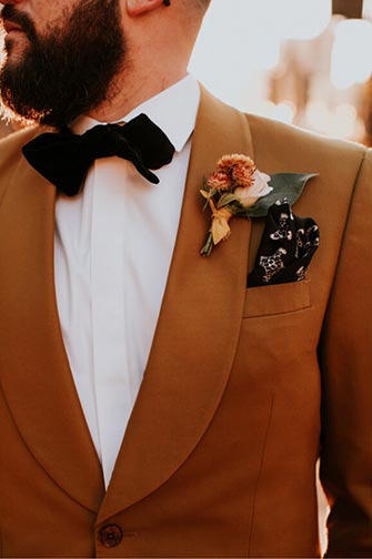 groom in gold suit jacket and black bow tie with flower lapel 