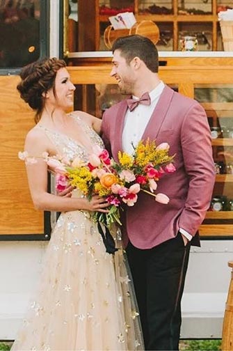 bride holding flower bouquet with arm around groom in pink suit jacket