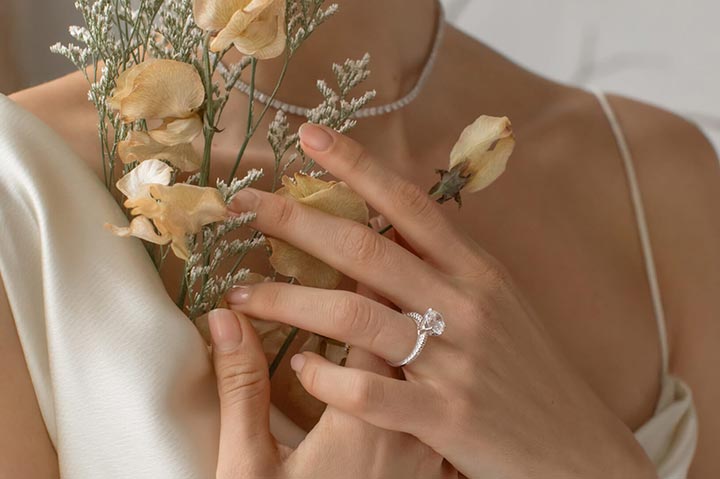 woman wearing an engagement ring and holding flowers to chest