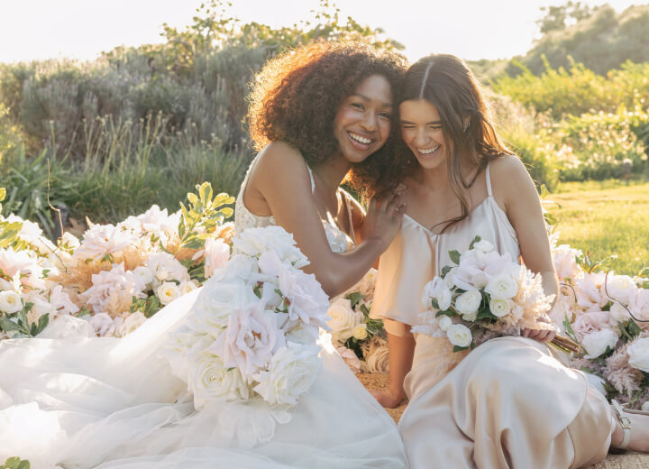 two brides sitting in a field with flower bouquets
