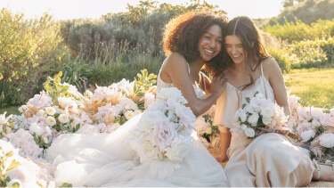 two brides sitting in a field with flower bouquets