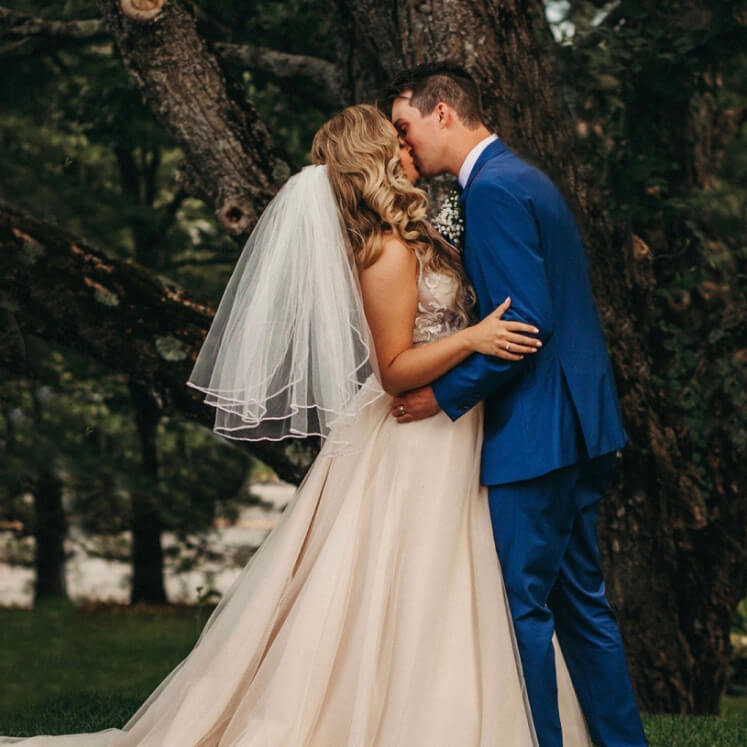 bride in a veil and wedding dress kissing groom in a blue tuxedo