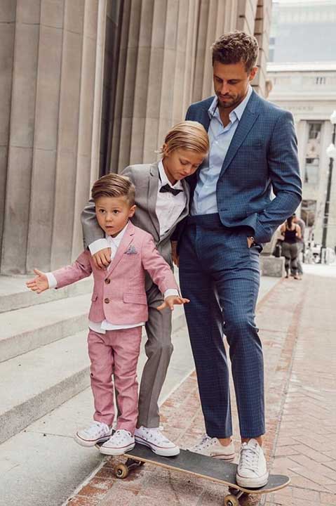 man wearing a navy suit standing on a skateboard with two boys wearing pink and gray suits