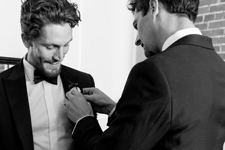 groomsman pinning flower on to groom wearing a bow tie and tuxedo