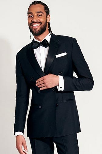 man wearing black tuxedo and bow tie standing with hand on jacket