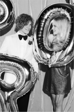 boy in a bow tie and tuxedo and girl in a prom dress standing with balloons